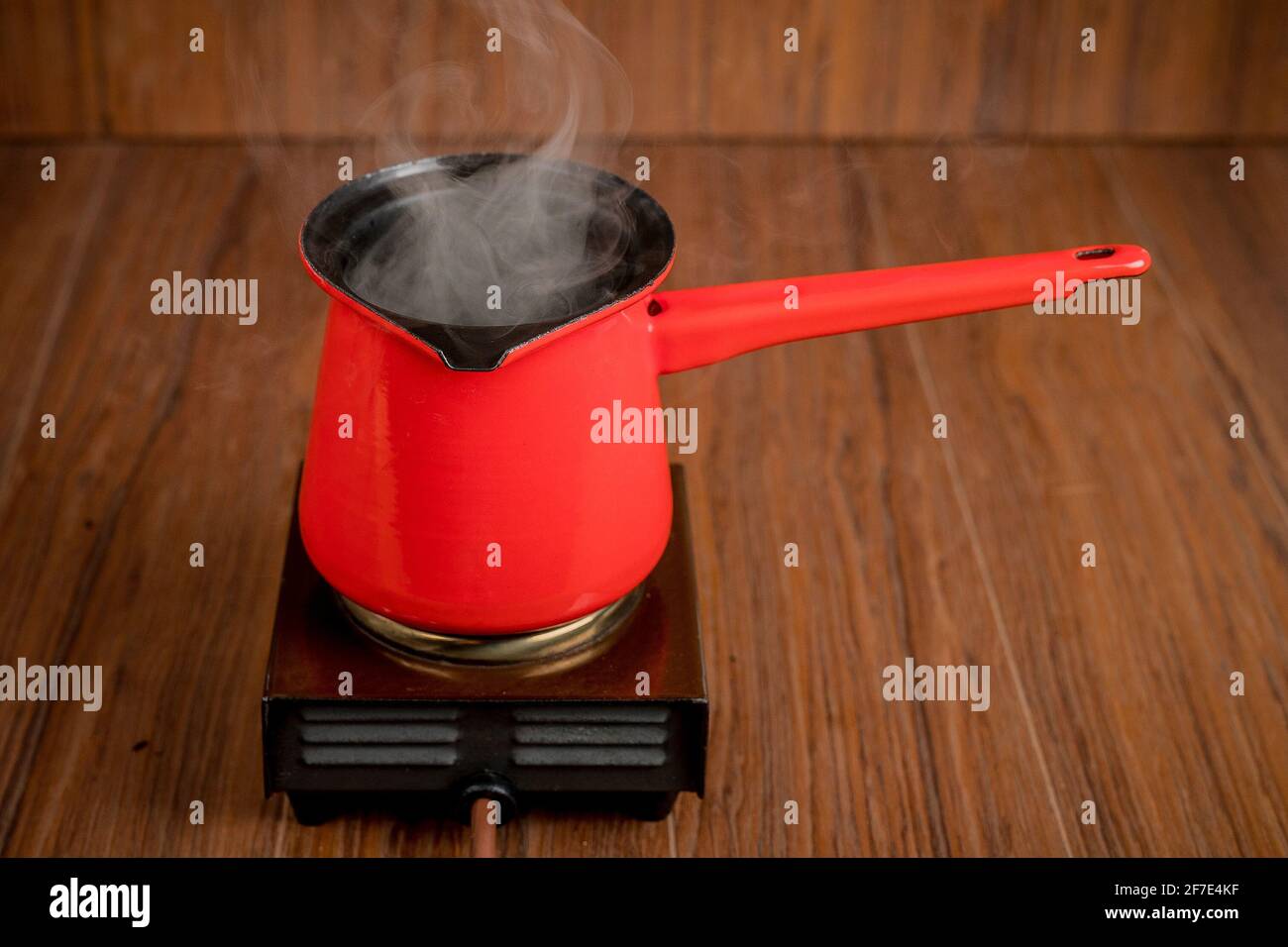 Petite cuisinière électrique mobile à plaque simple avec une cafetière rouge. De la vapeur ou de la fumée s'échappe de la cuve pendant la préparation du café ou d'une autre boisson chaude Banque D'Images