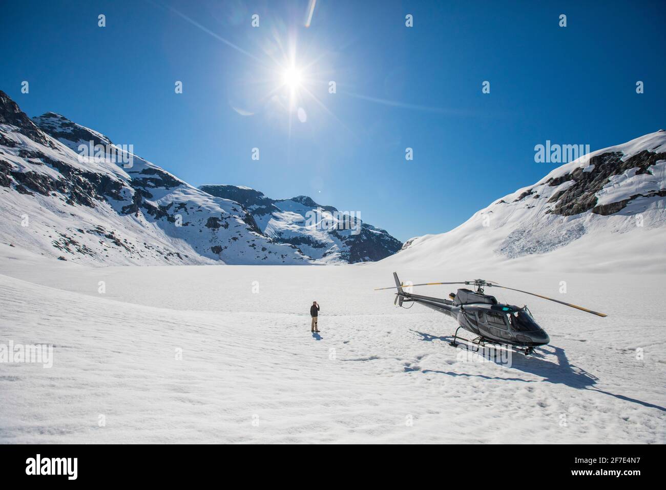 L'homme se tient à côté de l'hélicoptère et donne sur une vue panoramique sur la montagne. Banque D'Images