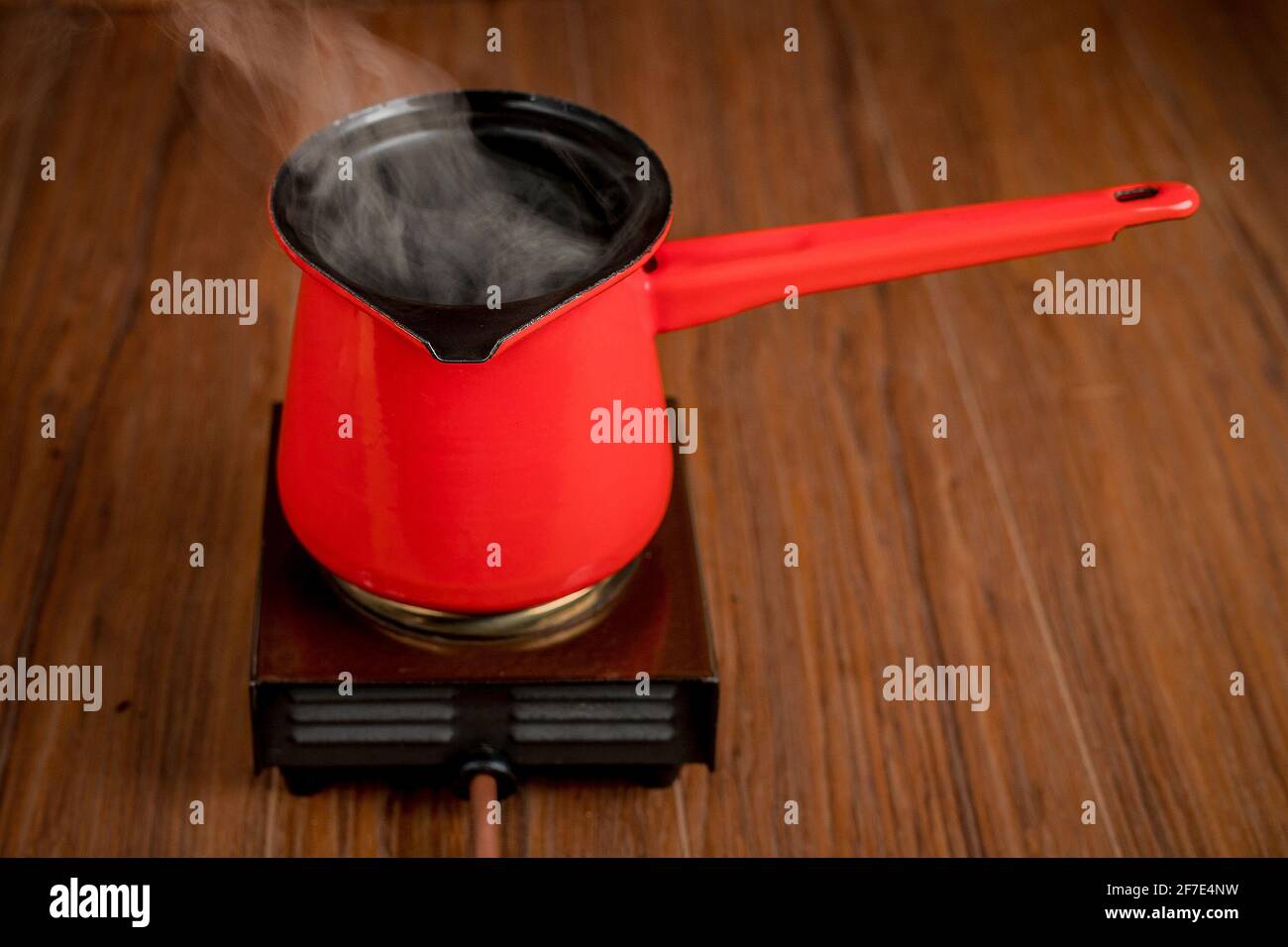 Petite cuisinière électrique mobile à plaque simple avec une cafetière rouge. De la vapeur ou de la fumée s'échappe de la cuve pendant la préparation du café ou d'une autre boisson chaude Banque D'Images