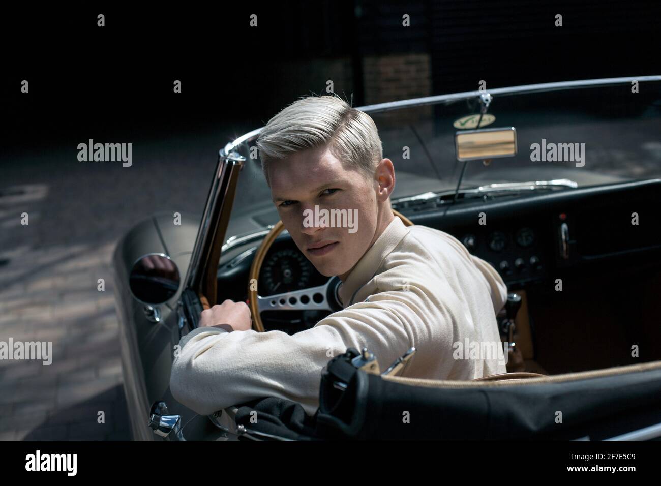 Jeune homme élégant sur une route avec voiture convertible classique regardant dans l'appareil photo , Angleterre . Banque D'Images