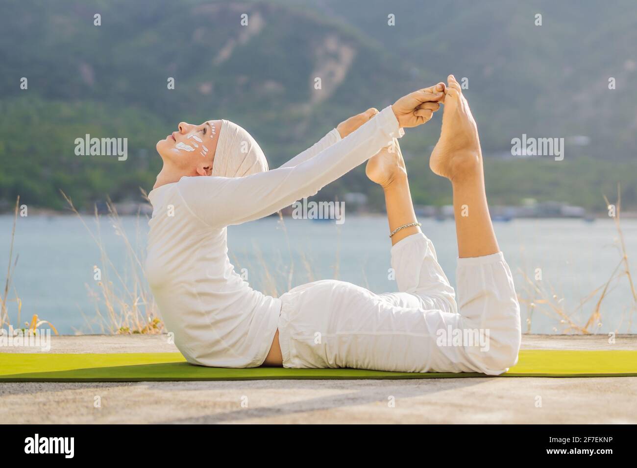 Kundalini yoga femme en vêtements blancs et turban pratique le yoga  kundalini sur le fond de la mer, des montagnes et du coucher du soleil.  Peinture de visage de combat Photo Stock -