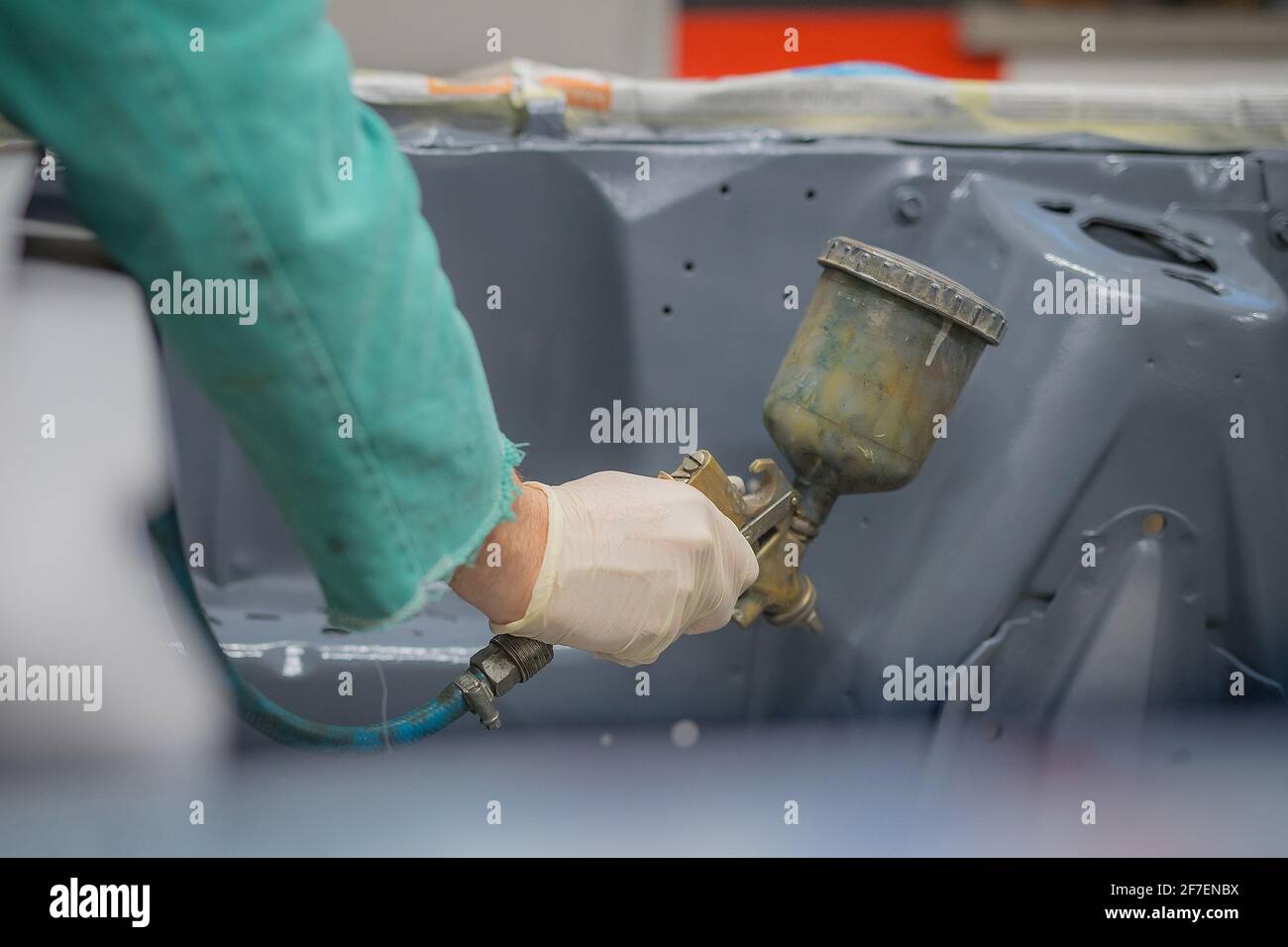 Homme en combinaison verte préparant un compartiment moteur d'une voiture pour une dernière couche de peinture. Homme pulvérisant du mastic liquide gris ou du stuc sur les panneaux de voiture en dernier Banque D'Images