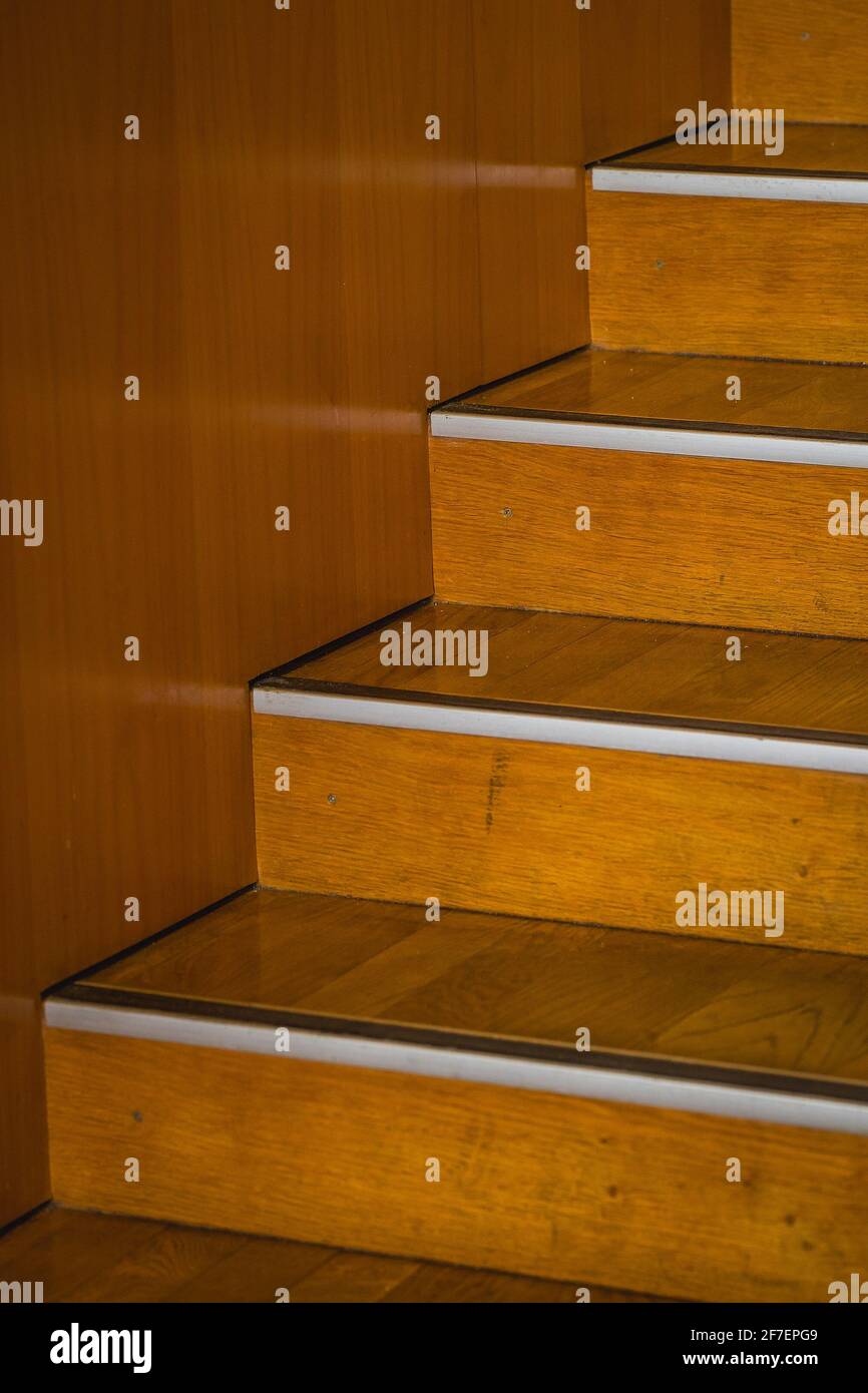 Détail des escaliers en bois, un peu usés, avec un bord d'attaque en aluminium, se levant vers la droite à côté d'un mur en bois. Banque D'Images