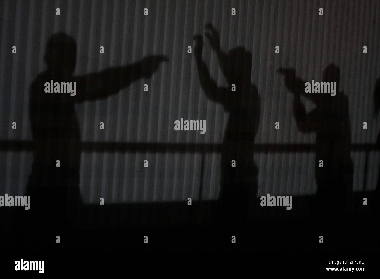 Silhouette de deux hommes inconnus tenant des armes à feu vers une autre personne sur un fond industriel gris. Banque D'Images