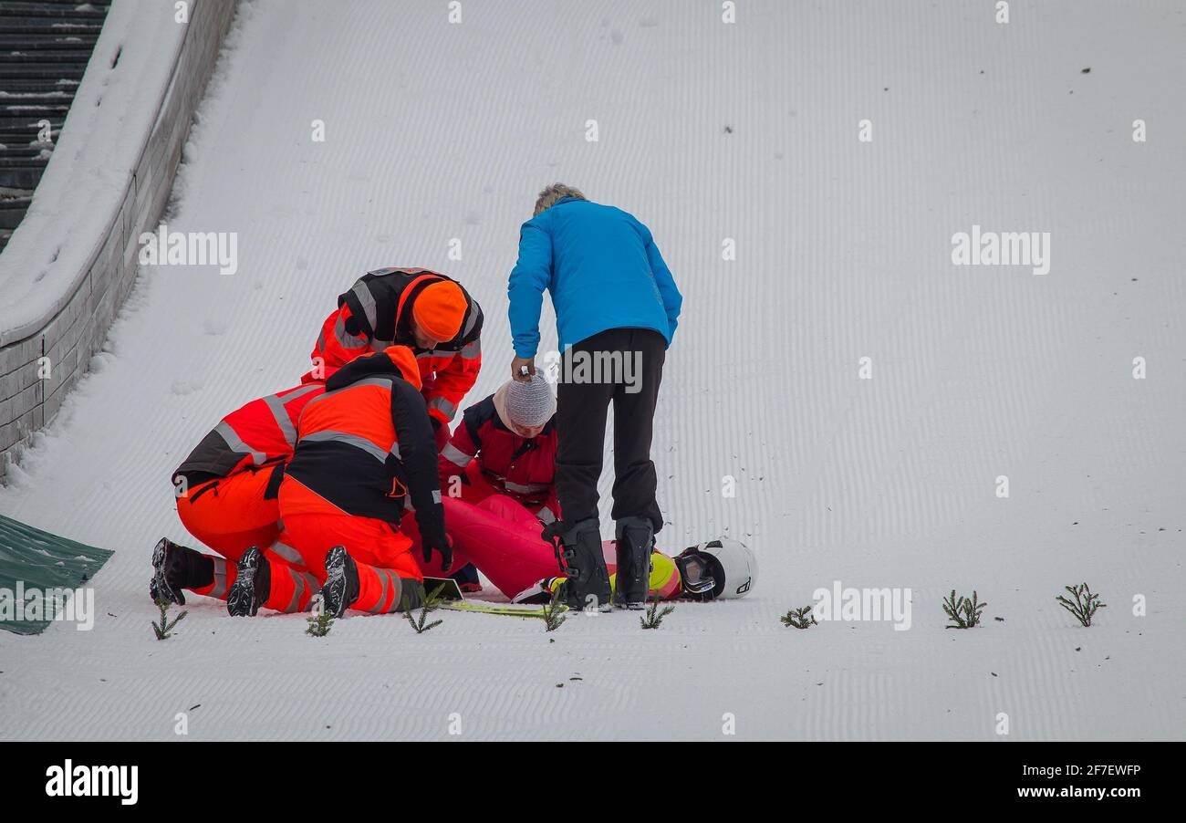 Ambulanciers paramédicaux et secouristes qui aident un cavalier blessé au fond du saut à ski. Cavalier blessé dans la douleur. Banque D'Images