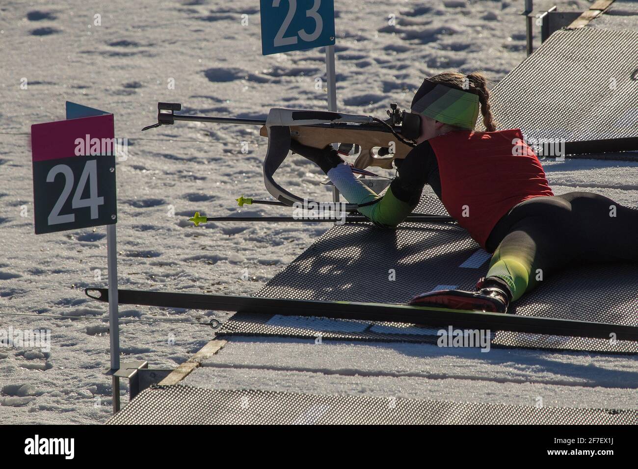 Une coureur de biathlon féminin est couché sur le sol et vise sa carabine. Femme biathlète sur un stand de tir, tirant couché. Banque D'Images