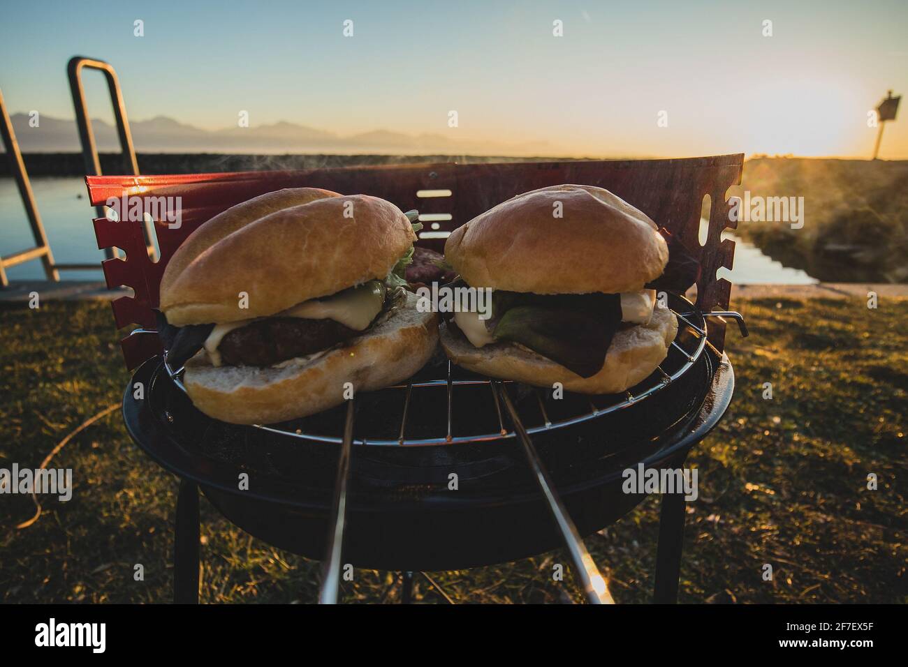 Griller des hamburgers sur un petit métal portatif au charbon de bois sur Les rives du Lac Léman en Suisse au début de l'hiver soirée avec coucher de soleil Banque D'Images