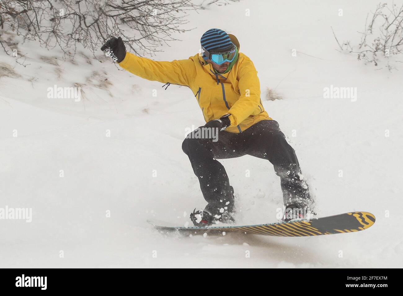 Un snowboardeur dans la neige descendant et sautant. Boarder avec des vêtements jaunes avec pantalon noir et planche orange à cheval et saut sur la neige sur un Banque D'Images