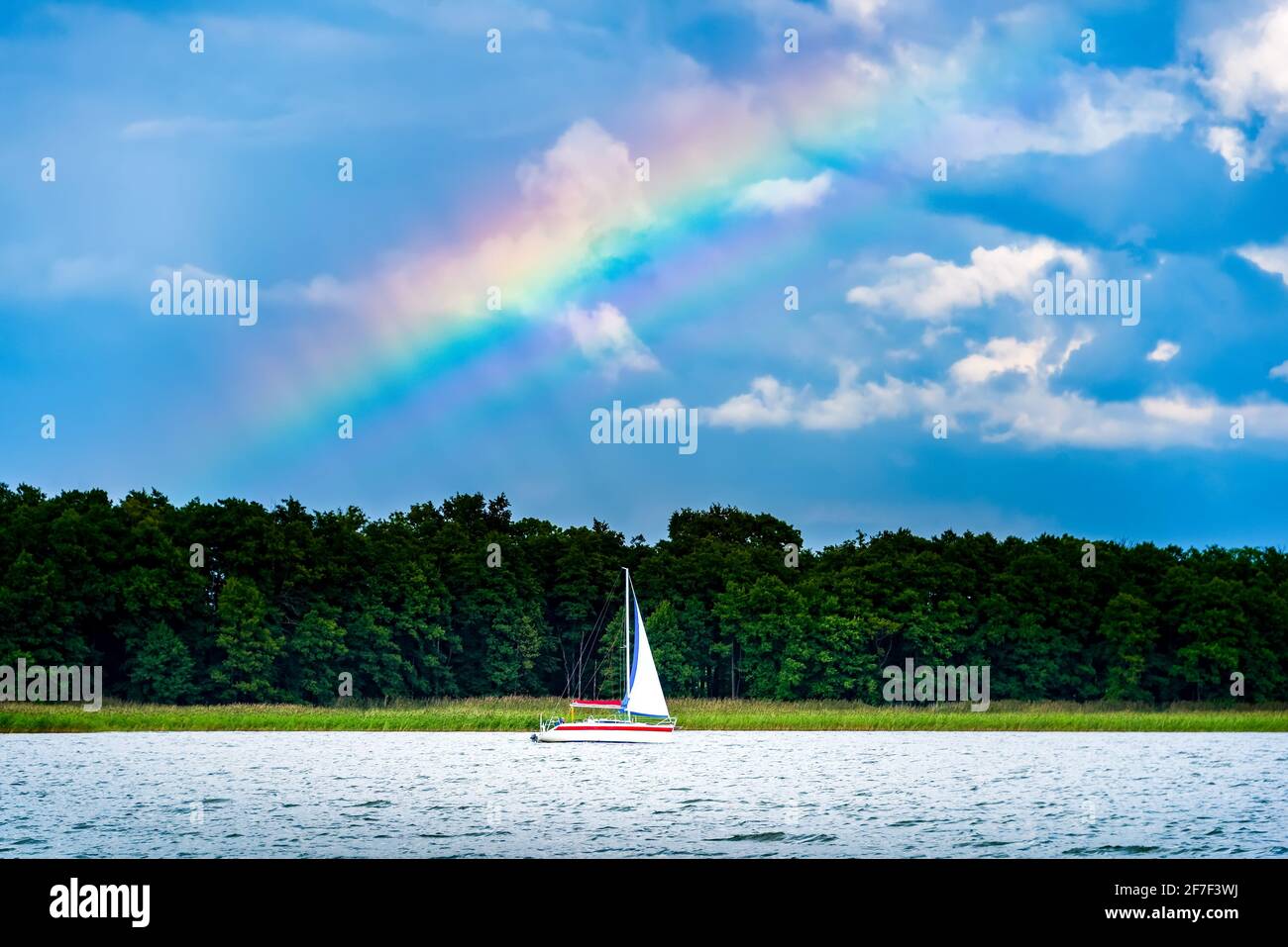 yacht avec voile blanc sur un lac contre le ciel bleu pluvieux sombre et l'arc-en-ciel. vacances d'été à voile Banque D'Images