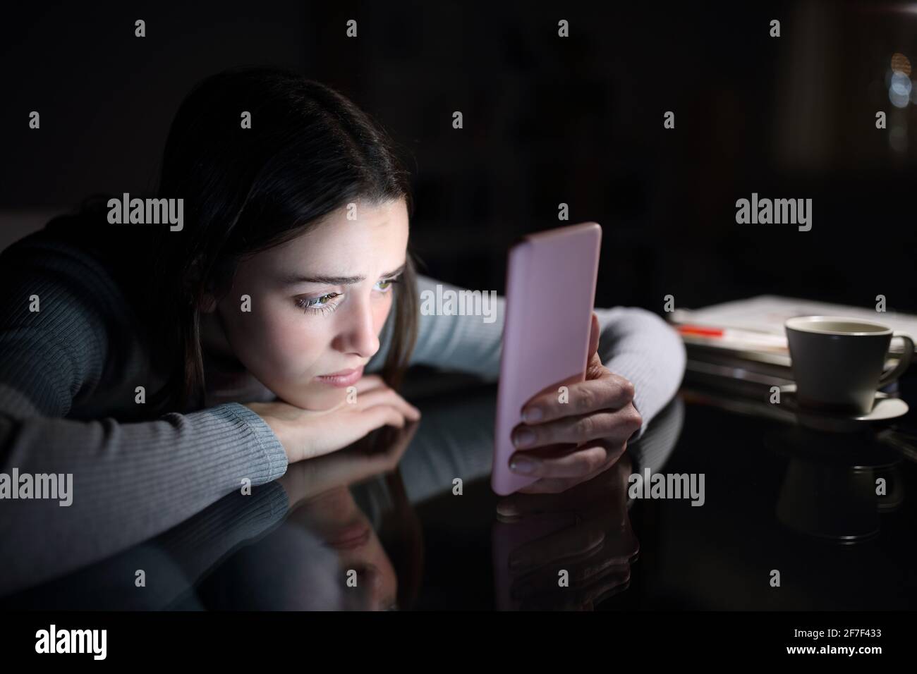 Triste femme qui vérifie le contenu d'un smartphone dans la nuit tombée à la maison Banque D'Images