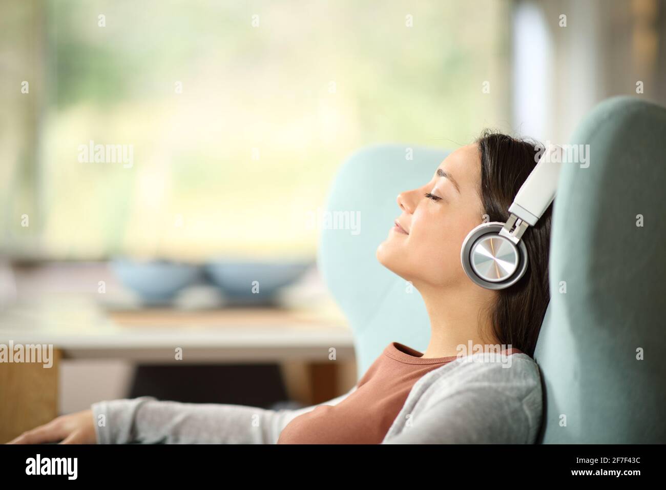 Portrait d'une femme décontractée portant un casque sans fil en vue latérale écouter de la musique sur une chaise à oreilles Banque D'Images