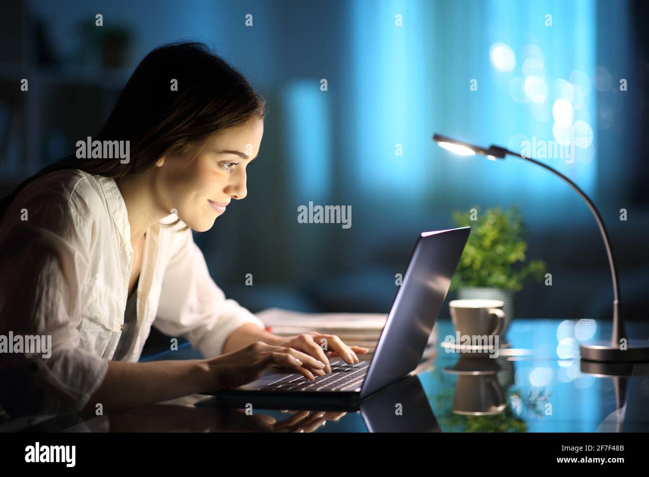 Bonne femme écrivant sur le clavier d'un ordinateur portable sur un bureau la nuit à la maison Banque D'Images