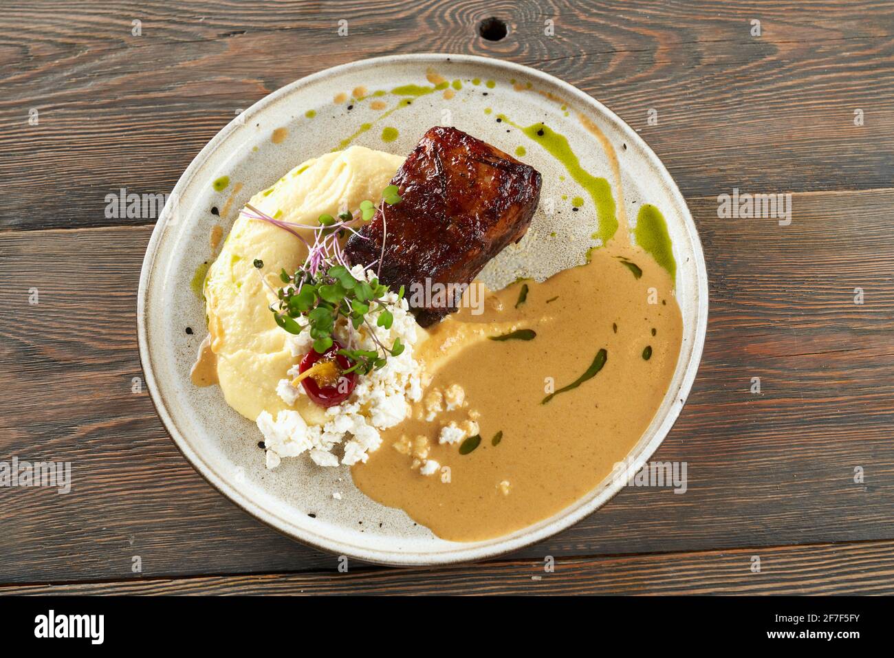 Vue d'en haut du steak de bœuf grillé juteux servi avec purée de pommes de terre, fromage cottage, sauce et pousses. Plat savoureux présenté sur une table en bois au restaurant. Concept de cuisine. Banque D'Images