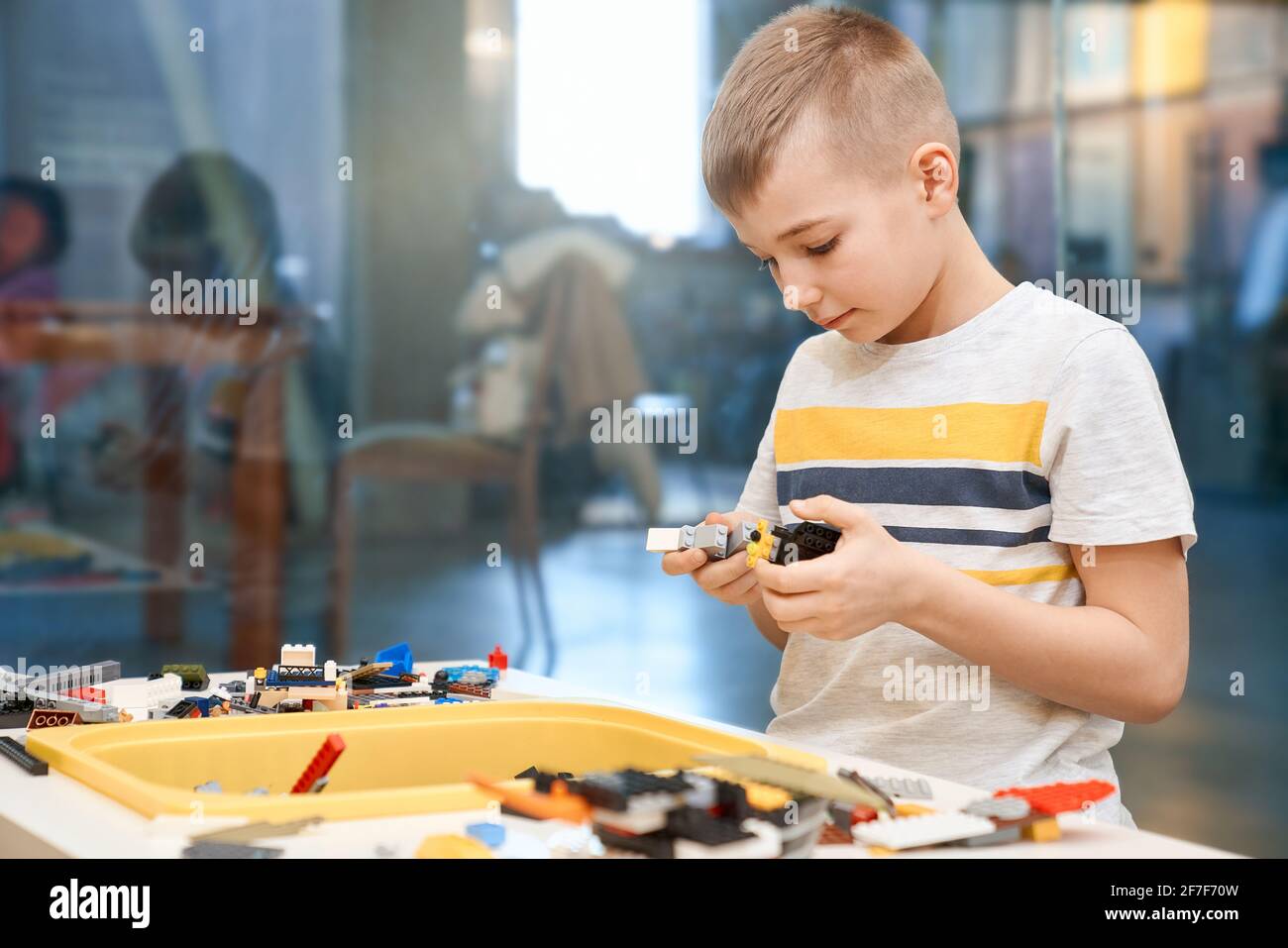 Vue de face du kit de construction pour le groupe d'enfants créant des jouets, ayant des émotions positives et de la joie. Attention sélective de charmant garçon caucasien travaillant sur le projet, prenant des parties colorées. Banque D'Images