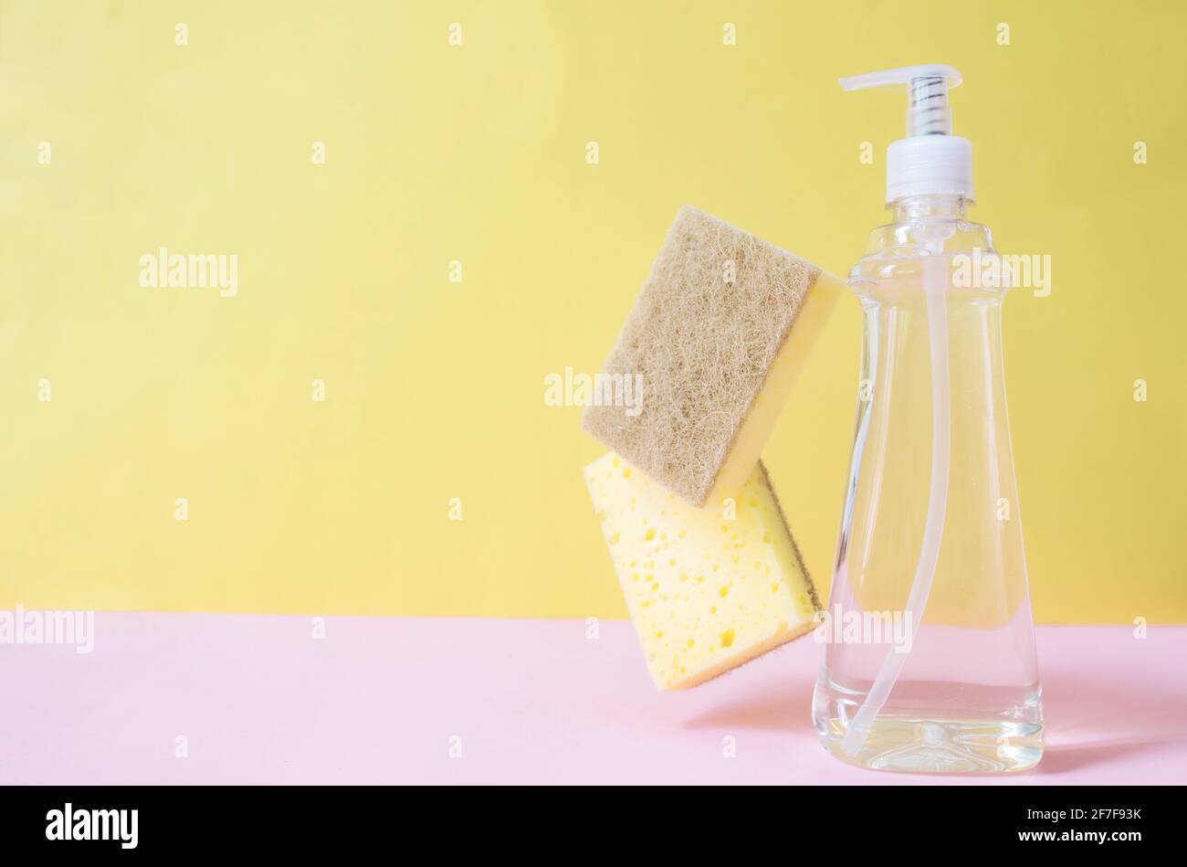 Poser à plat avec un compte-gouttes de savon, du liquide vaisselle, du savon à vaisselle, un débarbouillette sur fond rose pastel et jaune. Photo de haute qualité Banque D'Images