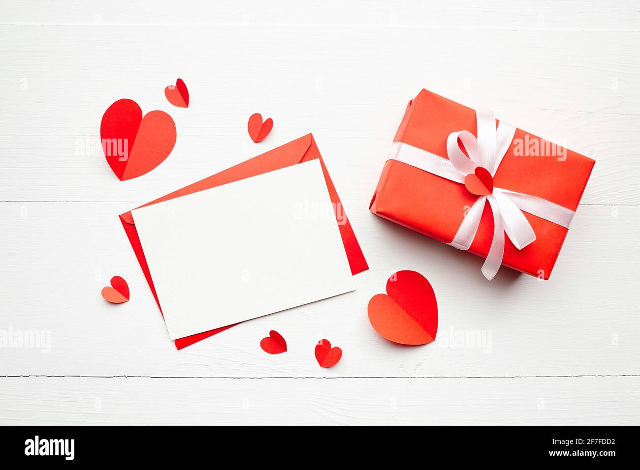 Carte de vœux de Saint-Valentin, posé à plat, vue du dessus. Maquette de carte de vœux, carte blanche vierge avec enveloppe et coeurs en papier rouge, boîte cadeau avec ruban Banque D'Images