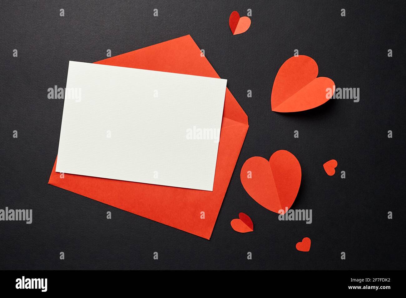 Maquette de carte de vœux avec décorations en papier sur fond noir, pose plate. Carte de vœux vierge de Saint-Valentin ou invitation, enveloppe et papier rouge il Banque D'Images