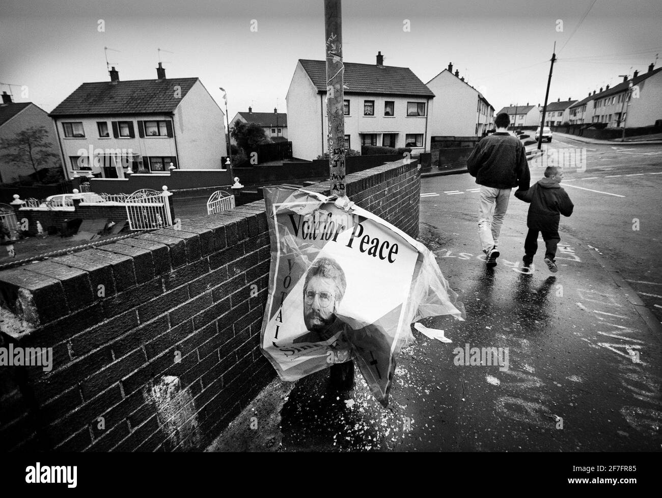 UN ÉLECTEUR ET SON FILS QUITTENT LE BUREAU DE VOTE EN PASSANT UNE AFFICHE TREMPÉE DE PLUIE DU LEADER DE SINN FEIN GERRY ADAMS DANS LA ZONE DE ROUTE DE SPRINGFIELD DANS L'OUEST DE BELFAST SCÈNE DE CERTAINS DES PIRES PROBLÈMES AU COURS DES 25 DERNIÈRES ANNÉES.PIC: BRIAN HARRIS Banque D'Images