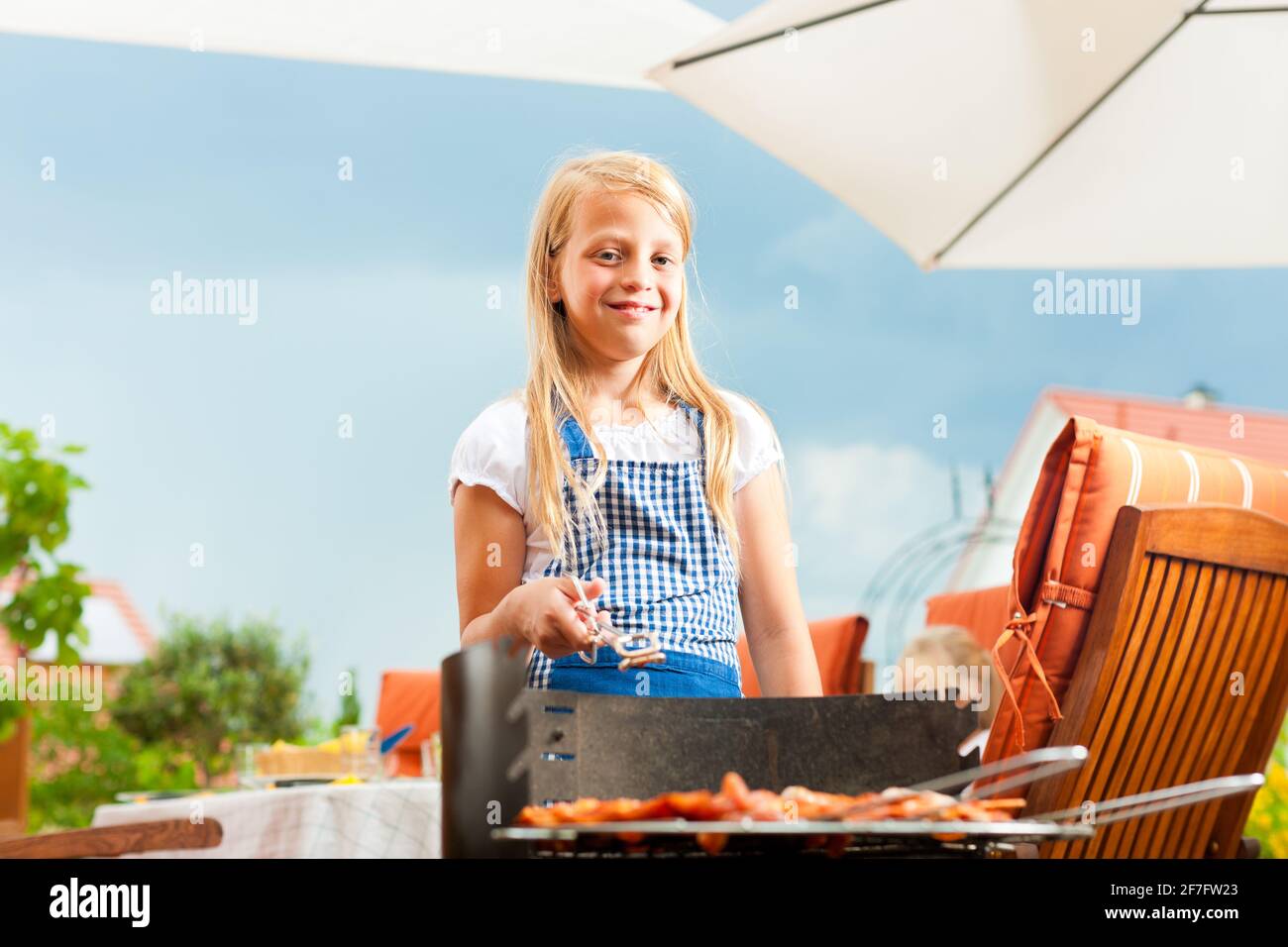 Bonne famille ayant un barbecue en été; la fille est debout au grill Banque D'Images