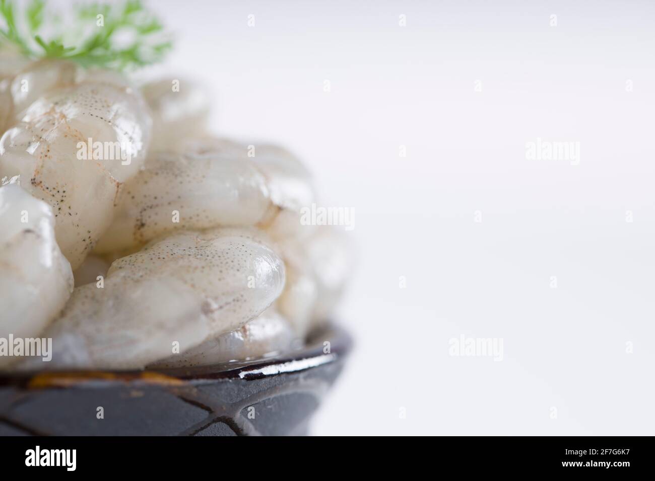 Crevettes pelées crues ou crevettes disposées en céramique noire petit pot et garni de feuilles de coriandre qui est prête pour cuisiner, placé sur une texture blanche Banque D'Images