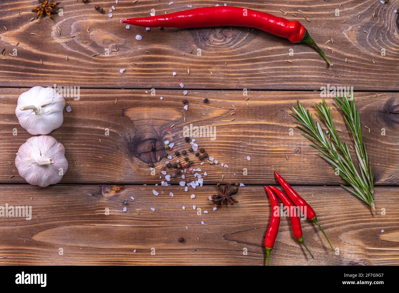 Piment, têtes d'ail, gros sel et romarin sur fond brun bois. Banque D'Images