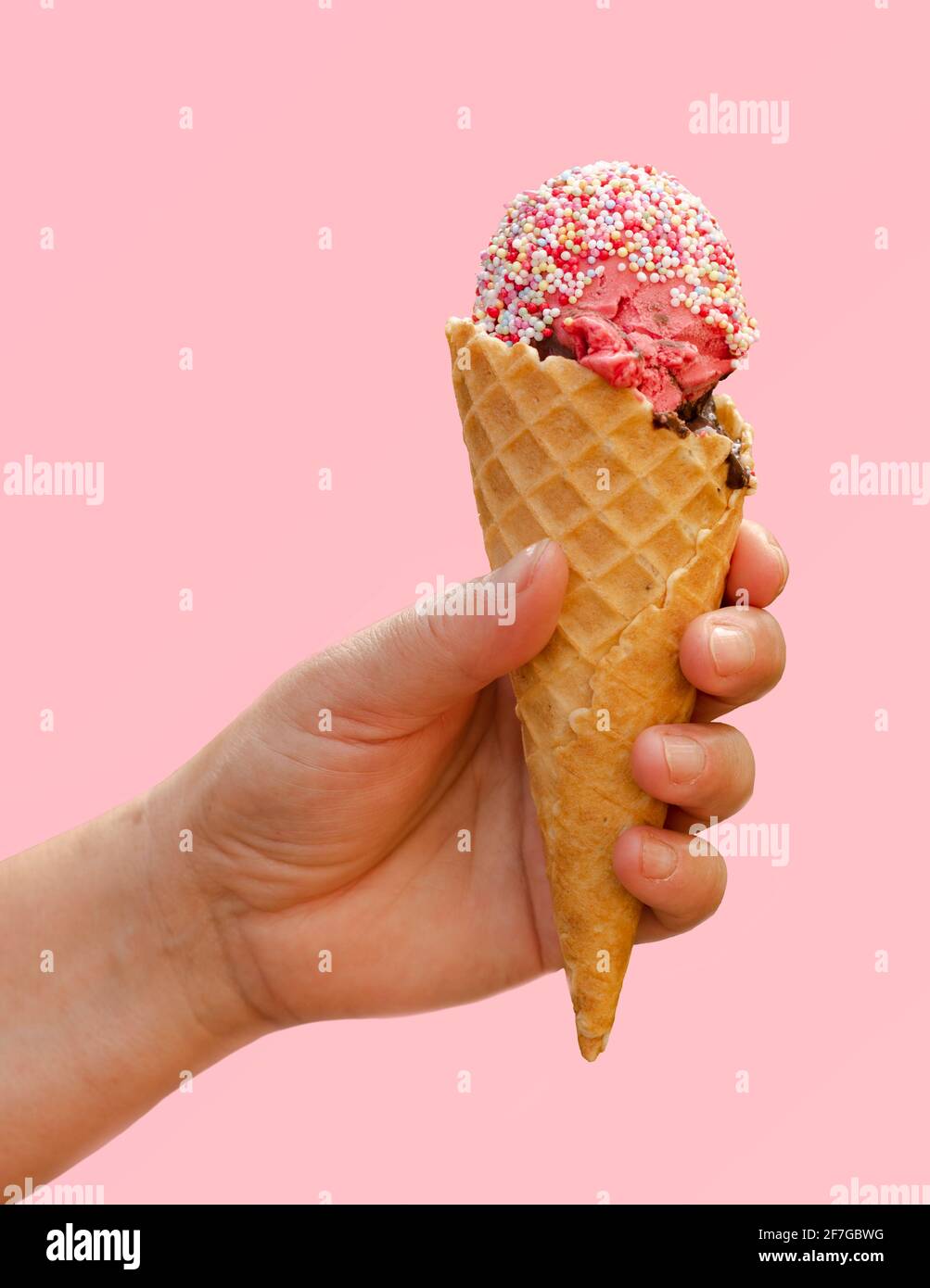 Main tenant la glace de fraise dans le cône de gaufré avec des bonbons saupoudrés isolés sur fond rose clair, goût du concept d'été, dessert congelé Banque D'Images