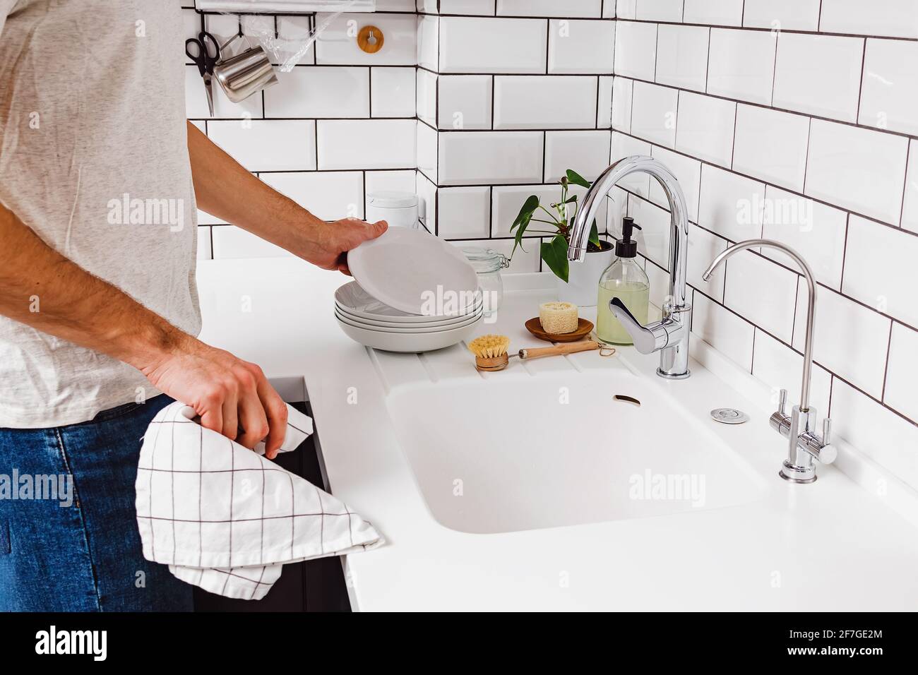 Un homme essuyant avec une serviette vaisselle dans la cuisine avec carreaux blancs. Banque D'Images
