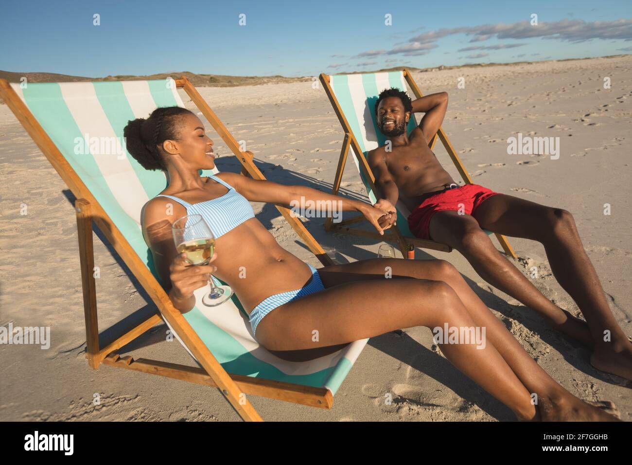 Couple afro-américain amoureux assis dans des chaises longues, tenant les mains sur la plage Banque D'Images