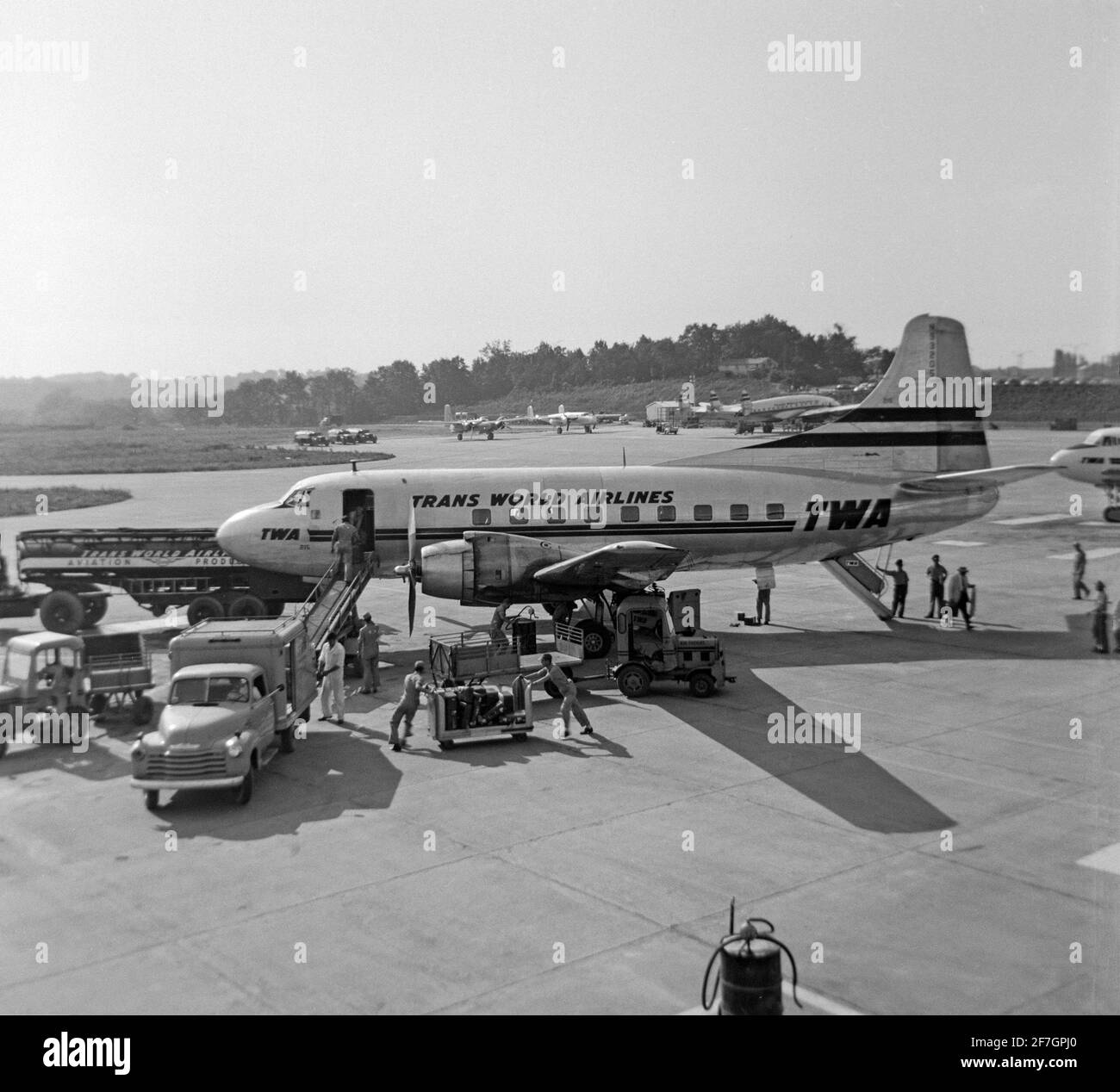 Une photographie en noir et blanc vintage de 1956 montrant un avion TWA, Trans World Airlines, Martin 202, numéro de série N93205, dans un aéroport aux États-Unis. L'avion est en préparation pour le vol et est entouré d'une variété de véhicules et d'ouvriers d'aéroport. Banque D'Images