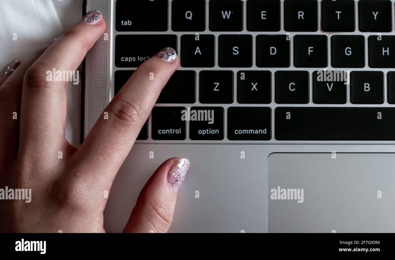 Les ongles peints à paillettes d'une femme appuient sur le bouton de verrouillage des majuscules d'un ordinateur personnel pendant une période de travail à la maison, février 2021. Banque D'Images