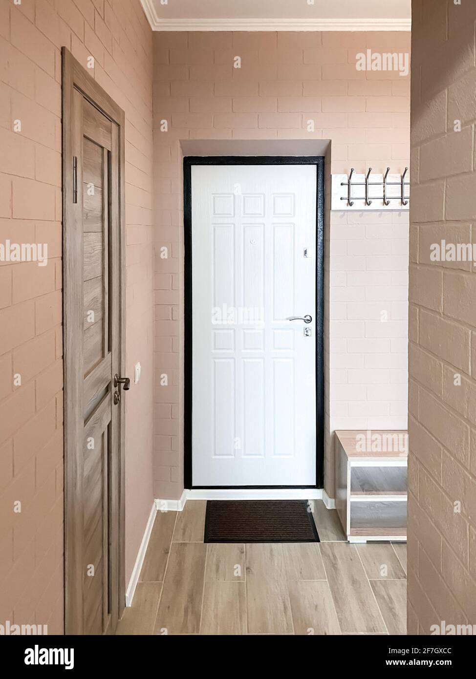Le design du couloir dans un petit appartement aux murs beige et à la texture brique. Porte avant blanche, armoire à chaussures, cintre à vêtements. Banque D'Images