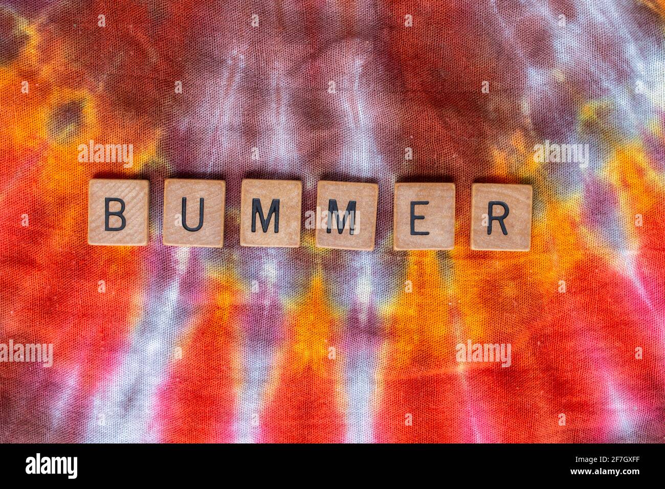 Le bummer est écrit en lettres de bois sur un fond textile de style hippie avec motif en rafale. Février 2021. Banque D'Images
