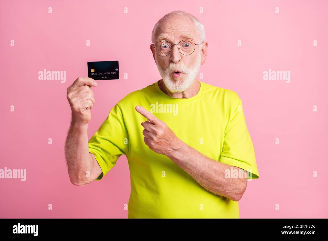 Photo de l'ancien choqué surprise surprise grand-père porter un t-shirt de lime point doigt carte de crédit isolée sur fond rose Banque D'Images