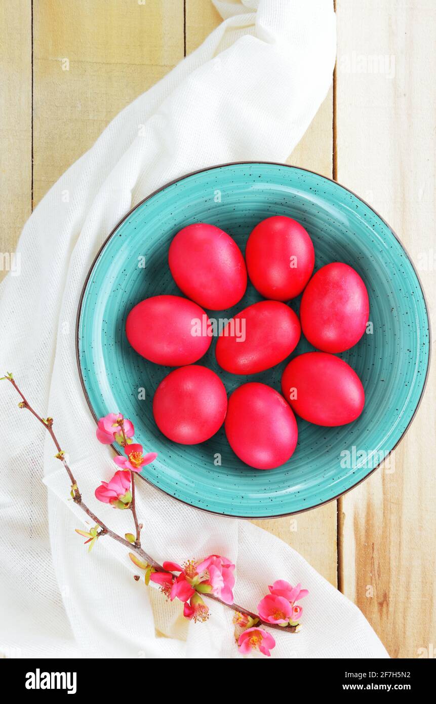 Bol turquoise avec œufs rouges et branche de coing à fleurs sur une table en bois Banque D'Images