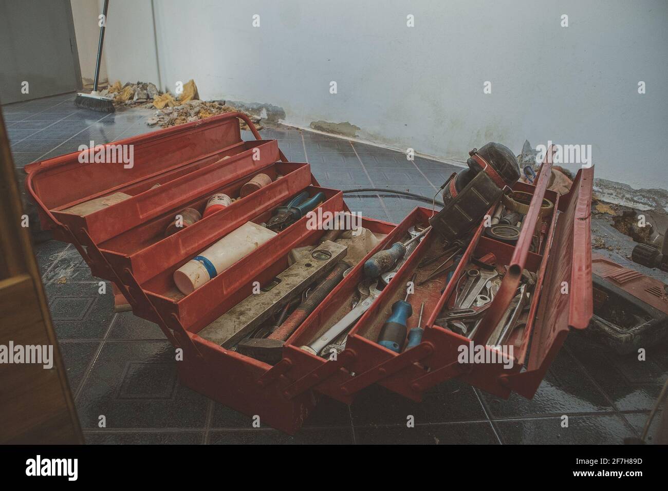 Ouvrez la boîte à outils rouge située au sol d'un chantier de construction dans un appartement. La boîte à outils contient des outils, des tournevis, des pinces, des clés, des tubes, etc Banque D'Images