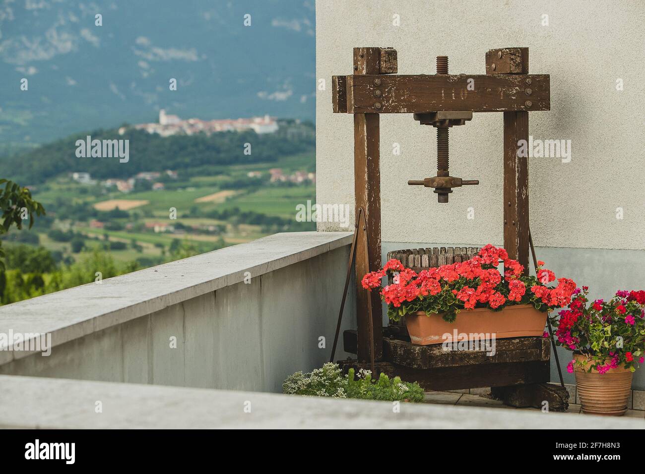 Une vieille presse à raisin pour faire du vin est debout sur un balcon avec une belle vue sur un vieux village sur la colline en arrière-plan. Banque D'Images