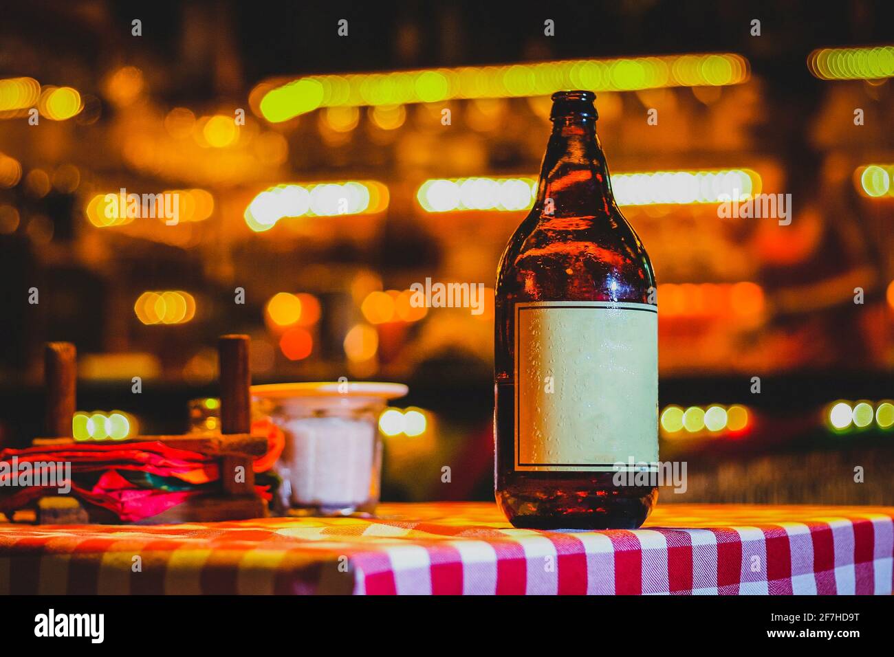 Bouteille de bière brune sur un fond coloré et lumineux dans un club ou un restaurant le soir. Photo d'un produit de style ambiant d'une bouteille de bière avec un autocollant blanc Banque D'Images