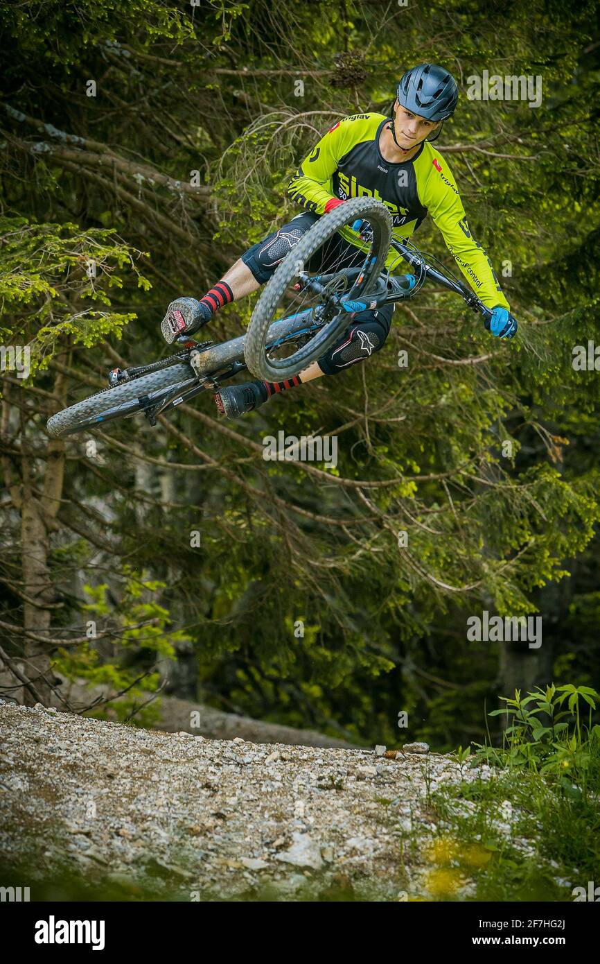 Photo frontale d'un alpiniste sautant sur un saut en terre dans un parc de vélo, entouré de forêt et d'arbres. Motard de montagne vert dans un environnement vert p Banque D'Images
