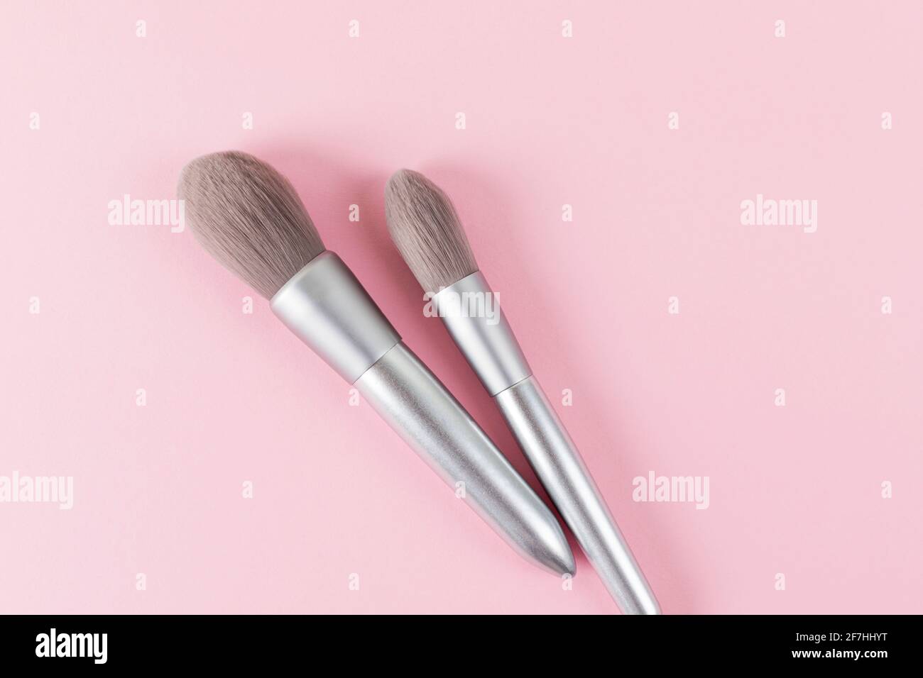 Deux pinceaux de maquillage professionnels couleur argent sur fond rose. Concept créatif de la beauté. Copier l'espace. Pose à plat. Banque D'Images