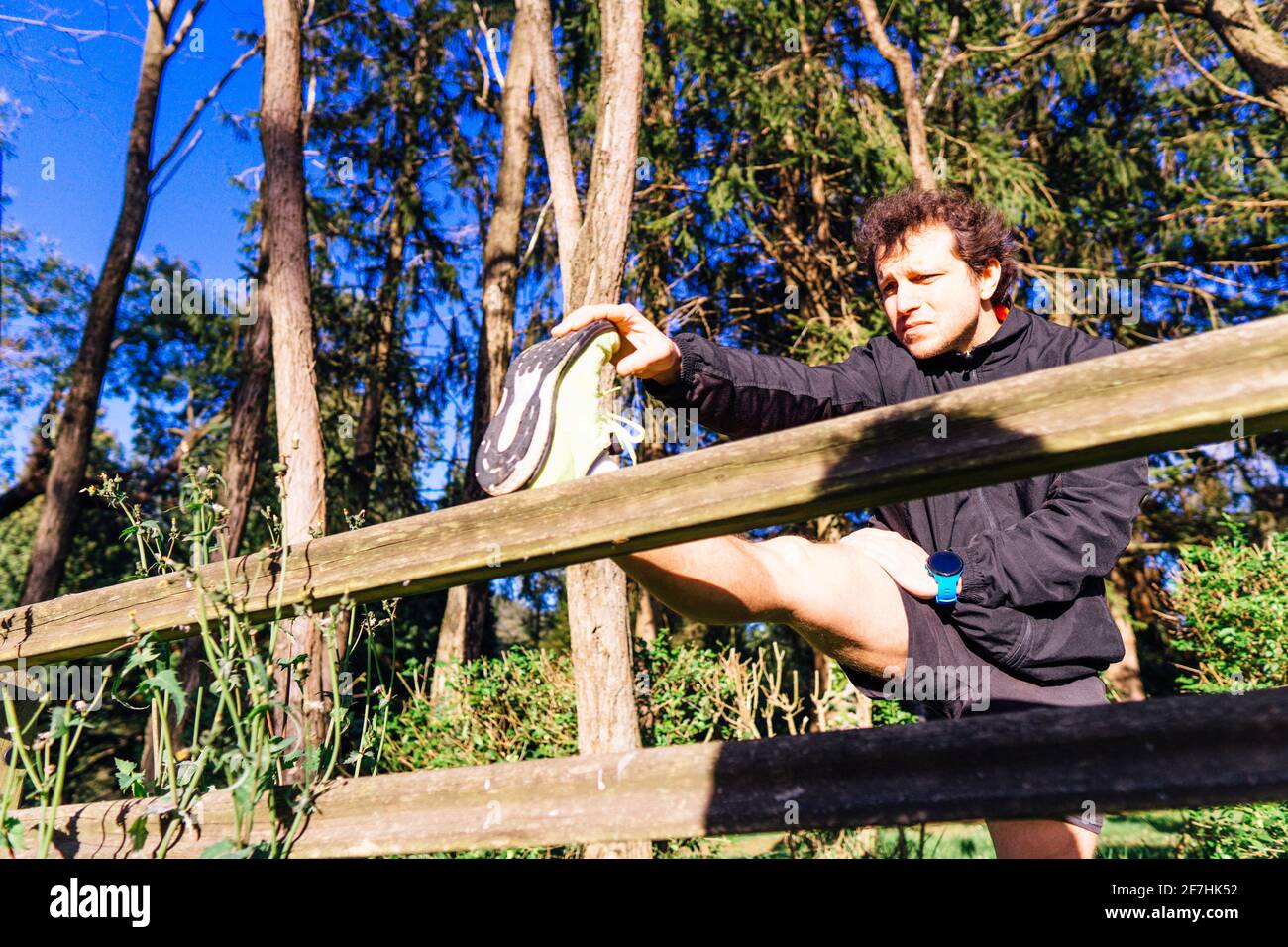 jeune homme adulte qui étire les cordes sur une rambarde en bois dans un parc boisé au coucher du soleil concept soins personnels étirage et sport Banque D'Images