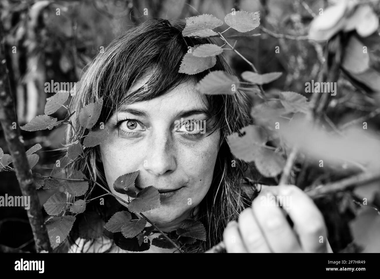 Portrait d'une femme en gros plan parmi les feuilles du parc. Photo en noir et blanc. Banque D'Images Portrait d'une femme en gros plan parmi les feuilles du parc. Photo en noir et blanc. Banque D'Images