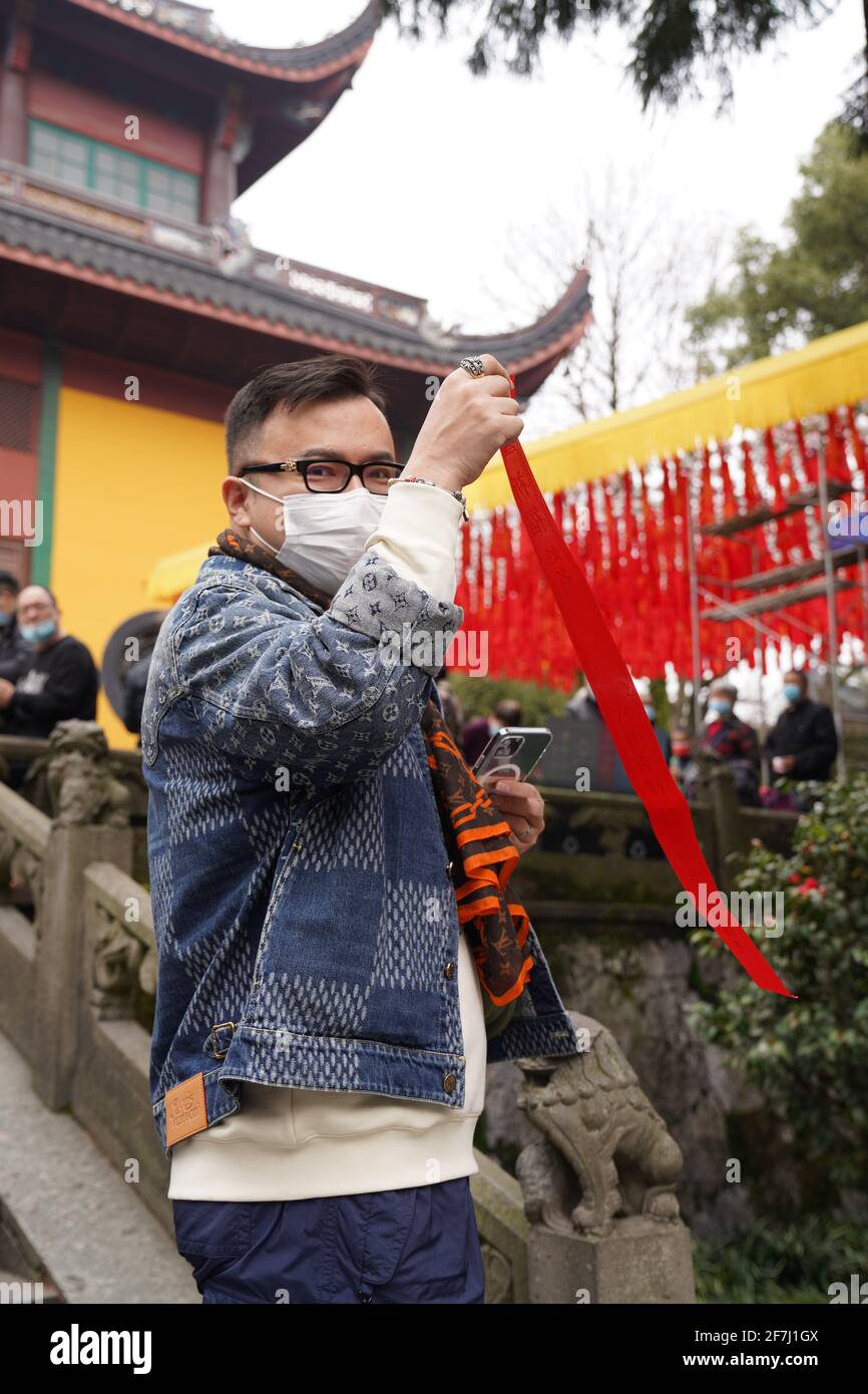 Un jeune homme avec masque facial prenant un ruban rouge pour la bénédiction de la nouvelle année devant le temple du bouddhisme. Banque D'Images