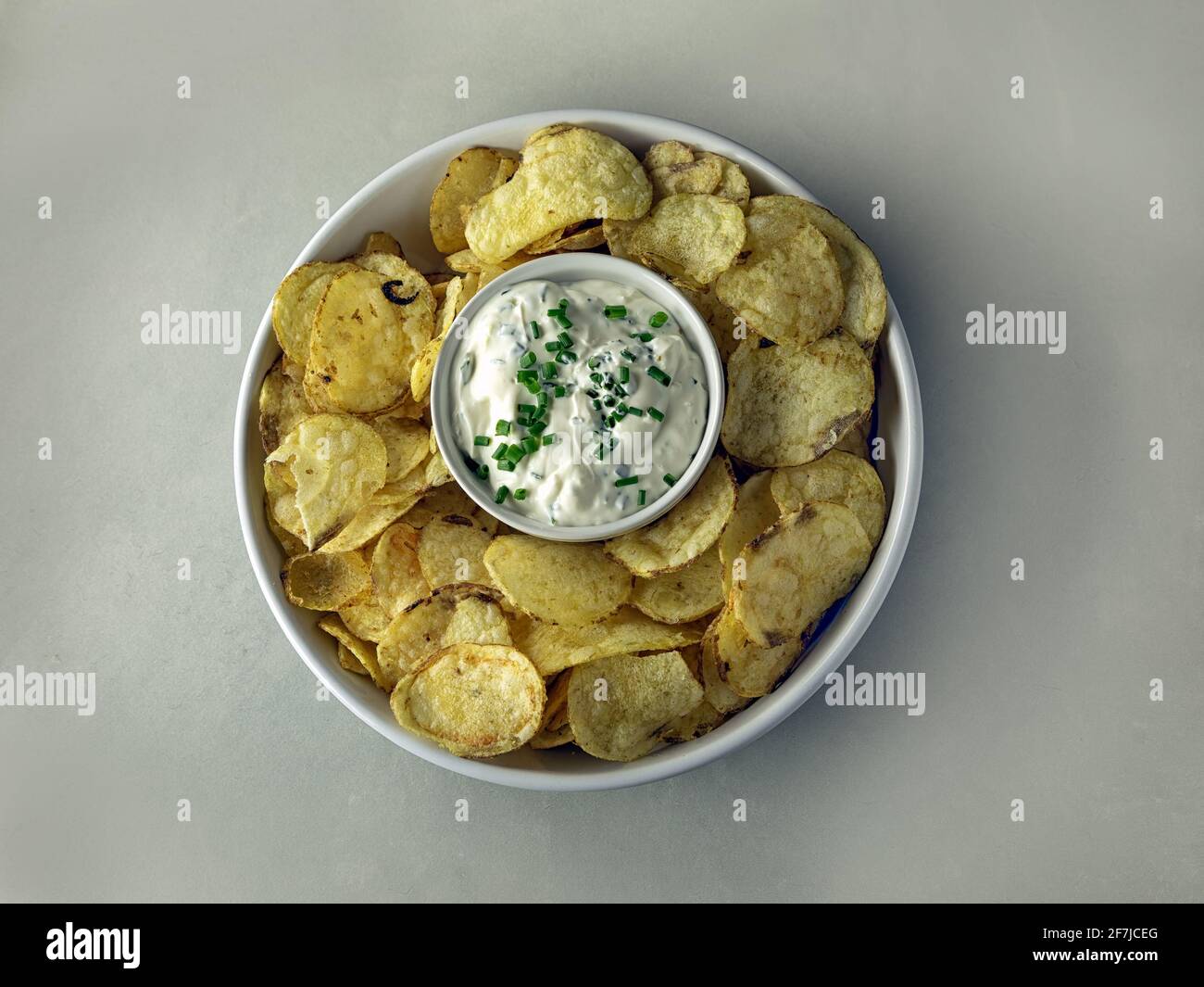 Vue de haut en bas d'un bol de chips de pommes de terre entourant un pot de crème aigre et de sauce à la ciboulette Banque D'Images