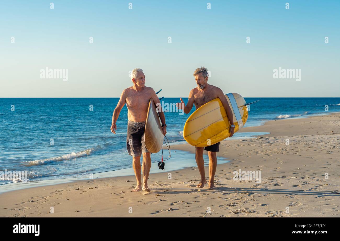 Deux hommes matures marchant avec des planches de surf sur la belle plage appréciant le paradis et le mode de vie de retraite. Une tenue attrayante pour les adultes Banque D'Images