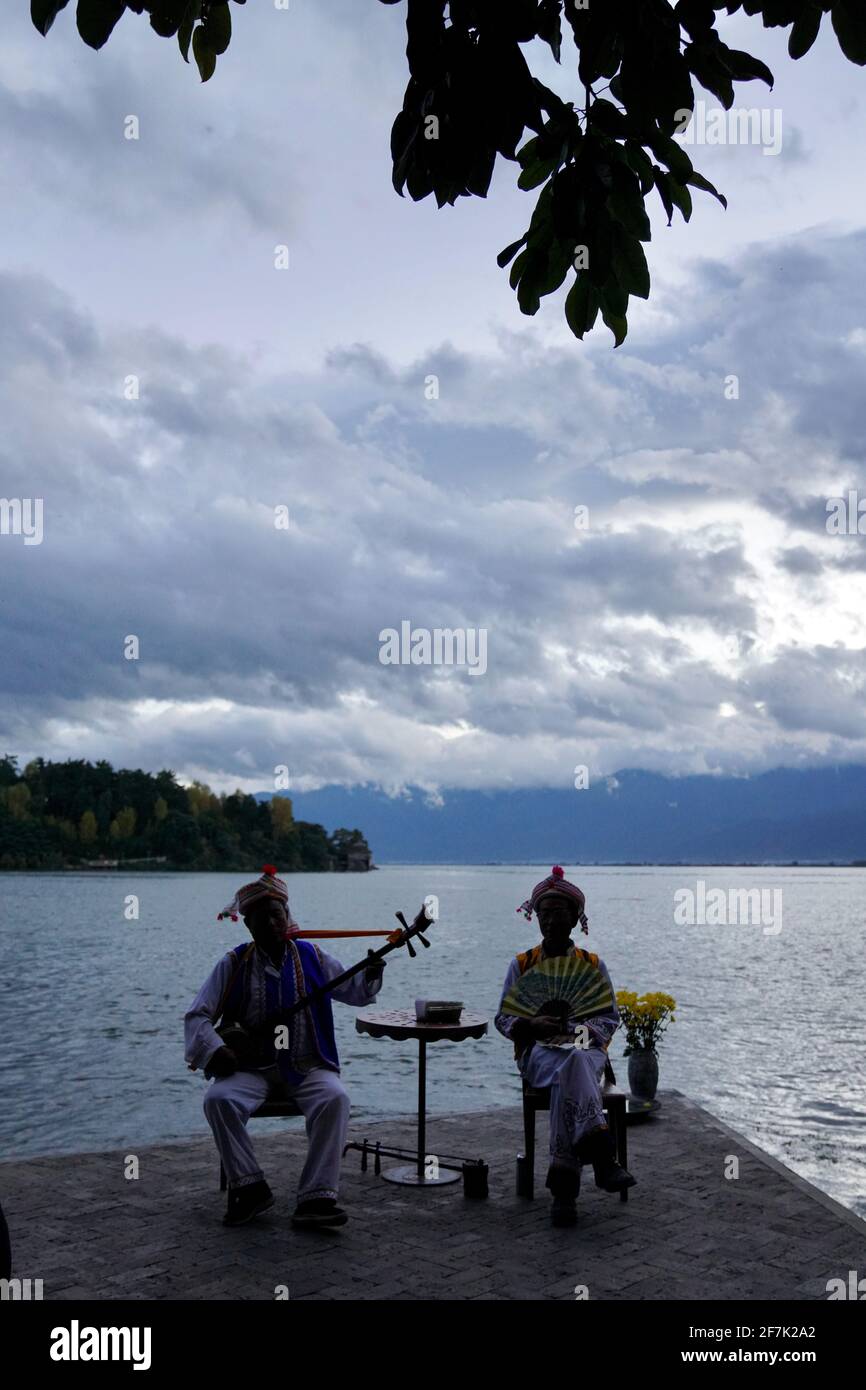 Deux hommes plus âgés s'habillant avec les gens traditionnels de Bai et Jouer des instruments de musique par Erhai lac avec nuageux et bleu tonifie le ciel pendant la nuit Banque D'Images