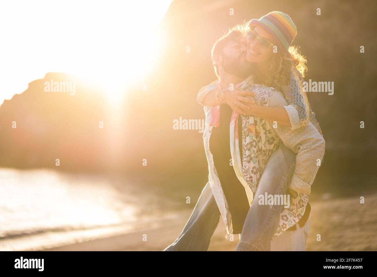 Couple caucasien adulte s'amuser ensemble dans le pigegyback - homme porter la femme et rire beaucoup avec l'amour et le bonheur à la plage avec coucher de soleil lumière incroyable Banque D'Images
