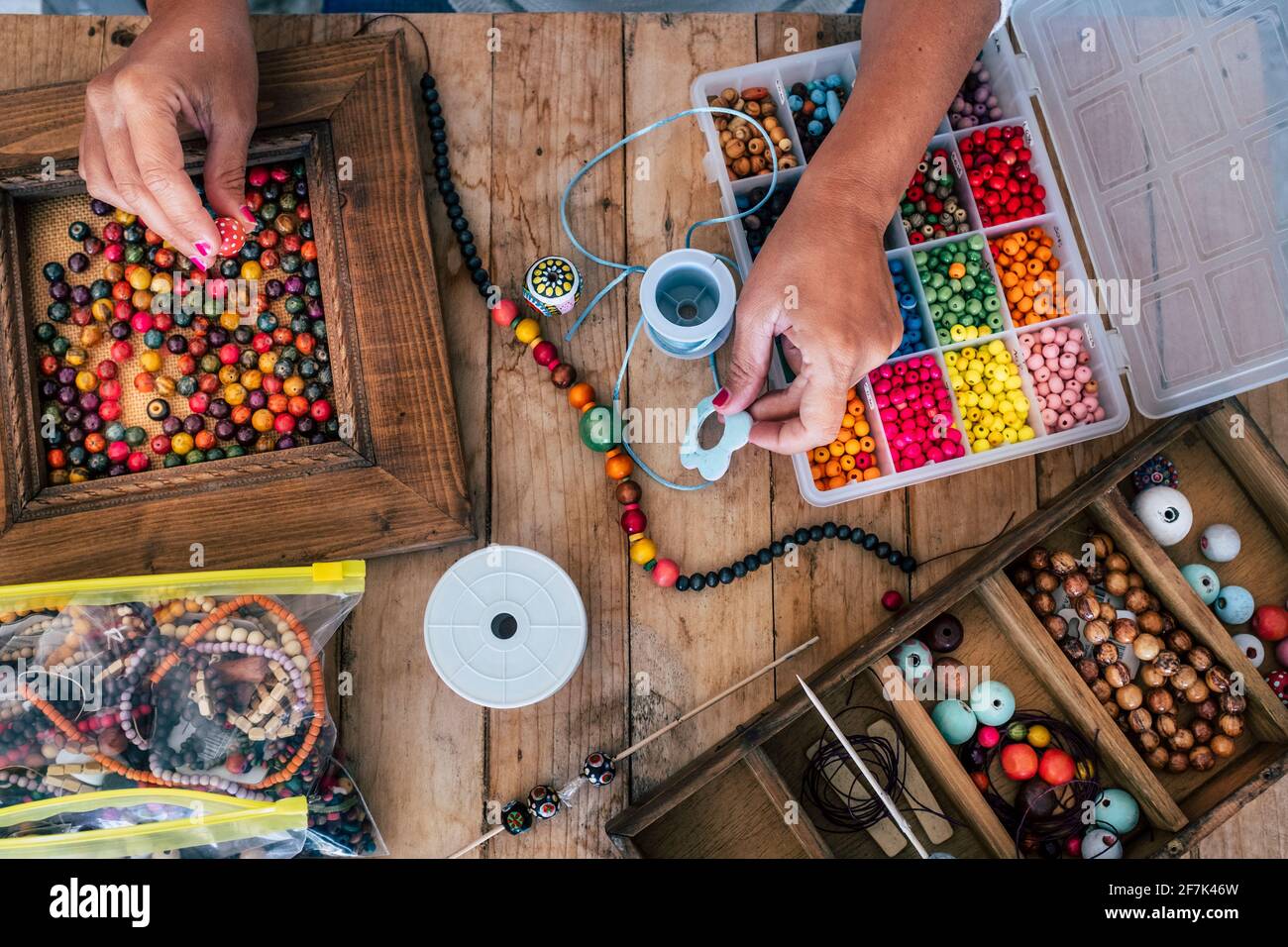Fabrication de bijoux faits à la main. Boîte avec perles sur une ancienne table en bois. Vue de dessus avec les mains de femme - tutoriel pour apprendre à faire des bracelets et des bijoux sur Banque D'Images