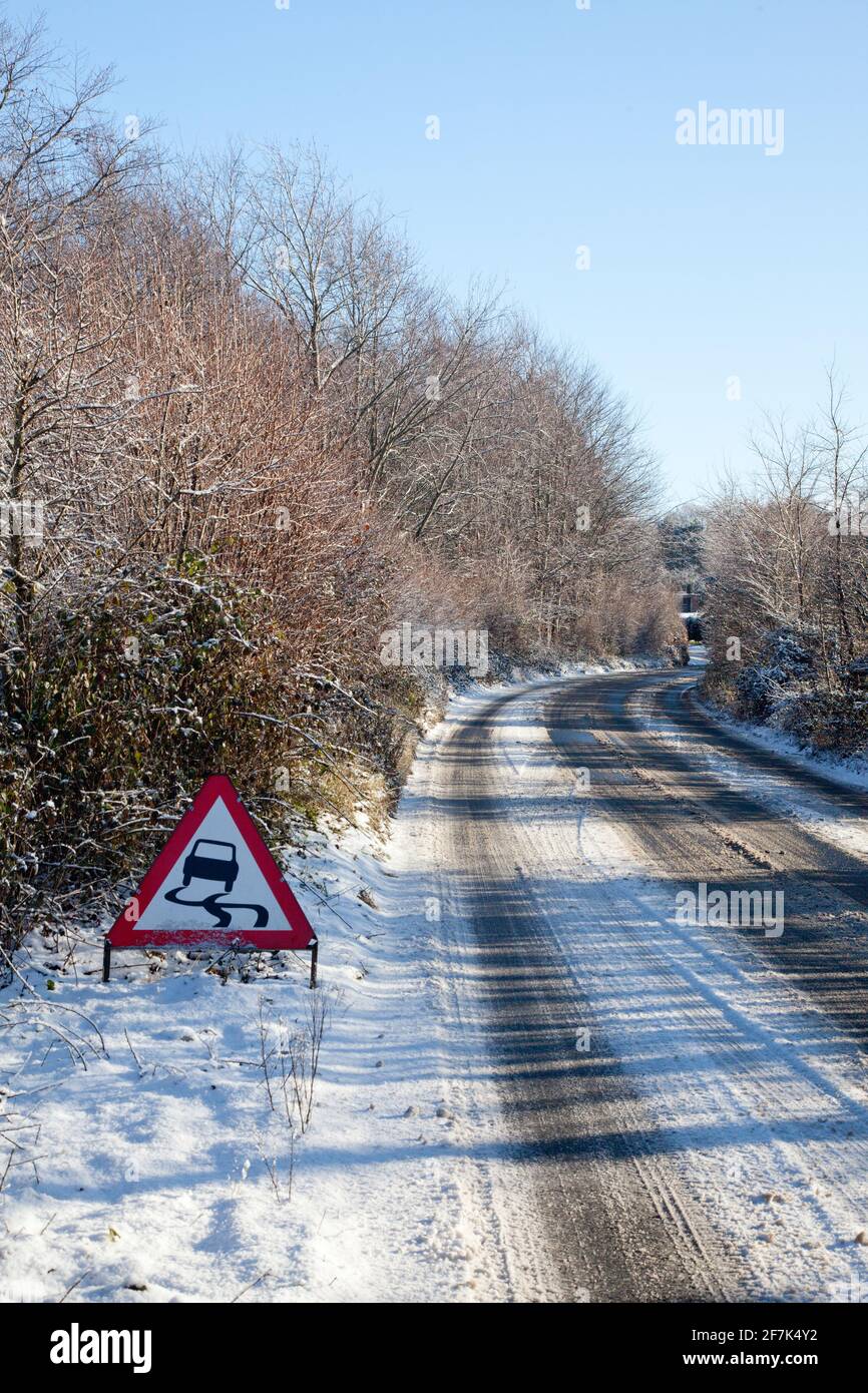 une route de campagne dans la neige par temps ensoleillé avec un panneau d'avertissement de chaussée glissante Banque D'Images