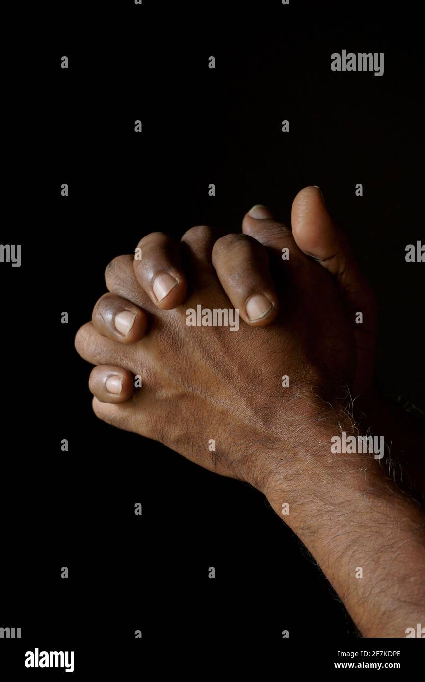Priant les mains de l'homme catholique indien isolé sur un fond noir. Banque D'Images