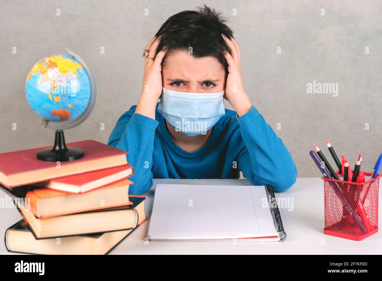 enfant en colère portant un masque chirurgical de protection, nourri avec le fait de faire devoirs en quarantaine sur fond gris Banque D'Images